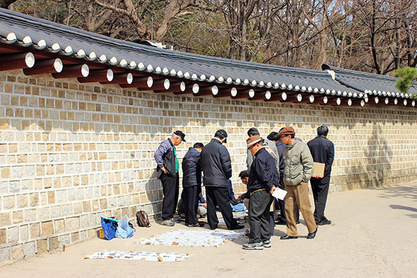 종묘 외곽 돌담벼락에 기대어 한가로이 장기를 두는 노년층의 일상 풍경